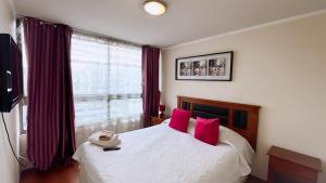 a bedroom with a bed with red pillows and a window at Apartamentos Bulnes in Santiago