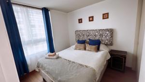 a bedroom with a bed with blue pillows and a window at Apartamentos Bulnes in Santiago