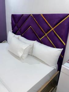 uma cama com almofadas brancas e uma cabeceira roxa em Bamod Hotel and Suites em Lekki