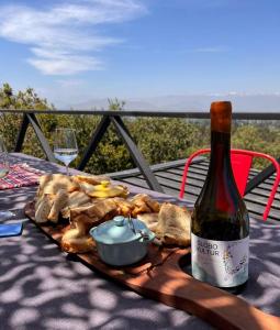 a bottle of wine and a plate of food on a table at Wine Lodge de Viña Vultur en bosque nativo con piscina in Doñihue