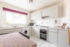 uma cozinha com armários brancos, uma mesa e um fogão em cosy 1 bedroom flat near Barking town centre em Barking