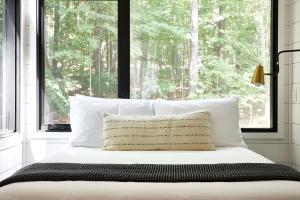 Una cama con almohadas blancas y una ventana con árboles. en AutoCamp Catskills en Saugerties
