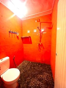 a bathroom with a toilet and a red wall at Garden Grove Guest House & Coffee Bar in Bukit Lawang