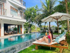 una mujer sentada en un banco junto a una piscina en HA Hotel Apartments Ocean Front en Hoi An
