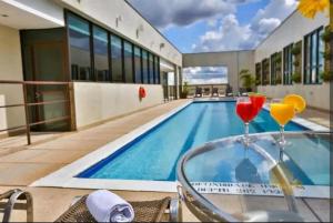 a swimming pool with two cocktails on a table next to a building at Flat aconchegante 5 andar in Brasília