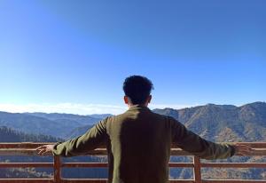 Ein Mann steht auf einem Geländer mit Blick auf die Berge in der Unterkunft Mountain and peace in Shimla