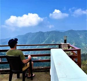 Ein Mann, der auf einem Stuhl sitzt und die Berge ansieht. in der Unterkunft Mountain and peace in Shimla