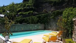 uma piscina com espreguiçadeiras ao lado de uma parede em Hotel Le Sully em Meyrueis