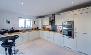 a large kitchen with white cabinets and a bar stool at Mariners Moon in Camber