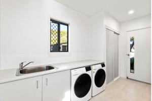 a white kitchen with a sink and a washing machine at Tranquil Getaways On Obi Maleny in Maleny