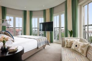 a bedroom with a bed and a couch and windows at Rocco Forte The Charles Hotel in Munich