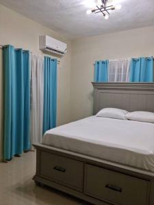 a bedroom with a bed with blue curtains at S.G Apartment Complex. in Linstead