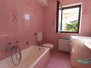 uma casa de banho cor-de-rosa com uma banheira, um WC e uma janela. em Nice apartment with terrace and grill for use em Malinska