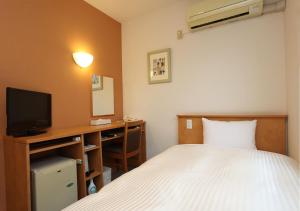 a bedroom with a bed and a desk with a television at Business Hotel Isesaki Heisei Inn in Isesaki