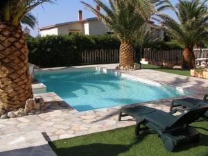 a swimming pool with a bench and palm trees at Modern Apartment in Valledoria with Swimming Pool in Codaruina
