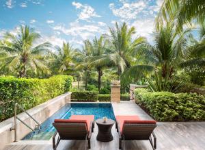 einen Pool mit 2 Stühlen und einem Tisch neben einem Resort in der Unterkunft JW Marriott Sanya Haitang Bay Resort & Spa in Sanya