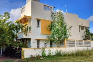 un bâtiment blanc et jaune avec des arbres devant lui dans l'établissement Athreyas@60/A, à Mysore