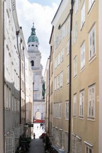 un callejón en la ciudad con una torre de reloj en el fondo en Altstadt-App. Domblick! en Salzburgo