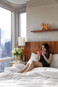 una mujer sentada en una cama mirando su celular en Hyatt Centric Times Square New York en Nueva York