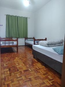 een kamer met 3 bedden en een houten vloer bij voltamos a funcionar casa da mãe Aparecida in Aparecida