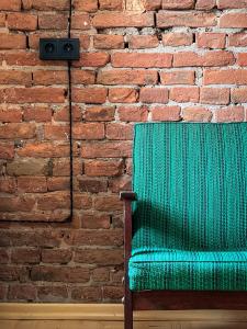 Black Tomato Hostel Kutaisi في كوتايسي: كرسي أخضر أمام جدار من الطوب