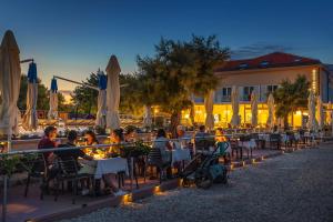 a group of people sitting at tables in front of a building at Hotel Dobrovit ex Tamaris in Baška