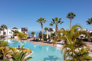 a large swimming pool with palm trees and the ocean at Las Terrazas de Abama Suites in Guía de Isora
