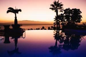 a swimming pool with palm trees and a sunset at Las Terrazas de Abama Suites in Guía de Isora