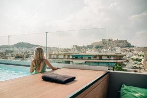 a woman sitting on the edge of a rooftop swimming pool at Athesense Suites in Athens