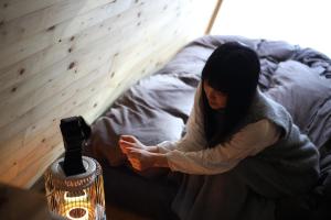 A-frame cabin iwor - Vacation STAY 36172v في Shimokawa: امرأة جالسة على سرير بجانب شمعة
