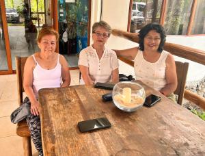 Natura Gardens Galápagos في Bellavista: ثلاث نساء جالسات على طاولة خشبية