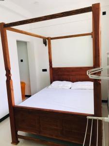 a bed with a wooden frame and white sheets at Roshan Villa in Weligama