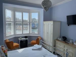 a bedroom with a bed and two chairs and windows at Lantana Guest House in Weymouth