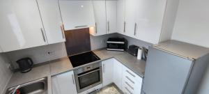 una pequeña cocina con armarios y electrodomésticos blancos en ExCel Exhibition Center Apartment, en Londres