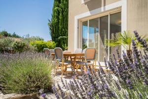 a wooden table and chairs in a garden with purple flowers at Villa Aprile in Saint-Étienne-du-Grès