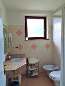 een badkamer met een wastafel, een toilet en een raam bij Hotel Al Caminetto in Cembra