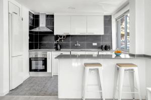 Bright Alges Apartment في ألجيس: مطبخ أبيض مع خزائن بيضاء وكراسي البار