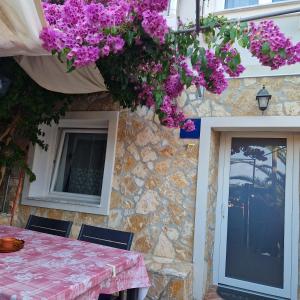 une maison en pierre avec une table et des fleurs violettes dans l'établissement Apartment Fay, à Mali Lošinj