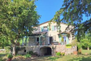 una grande casa in pietra con un portico e un albero di Chambres d'hôtes Le Muguet a Mandacou