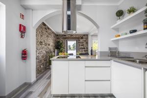 a kitchen with white cabinets and a stone wall at Basalt House A by Homie in São Vicente