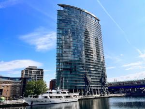a boat in the water in front of a tall building at The Canary Wharf Place - Stunning 2BDR Flat in London