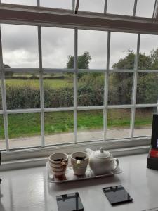 une table avec trois tasses sur une assiette devant une fenêtre dans l'établissement St Quintin Arms, à Harpham