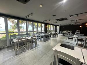 un restaurante con mesas y sillas blancas y ventanas en Ibis Joao Pessoa Praia, en João Pessoa