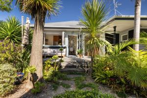a house with palm trees in front of it at The Country Beach Oasis in Papamoa
