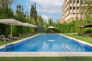 una piscina con sillas y sombrillas junto a un edificio en AC Hotel Sevilla Fórum by Marriott, en Sevilla