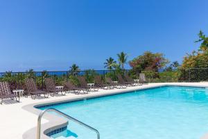 a swimming pool with chairs and tables and the ocean at Country Club Villas 302 in Kailua-Kona