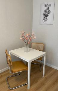 a white table and chair with a vase of flowers on it at Jūros apartamentai in Klaipėda
