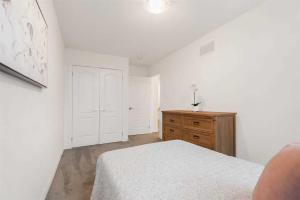 a white bedroom with a bed and a wooden dresser at Konia Suites in Orangeville