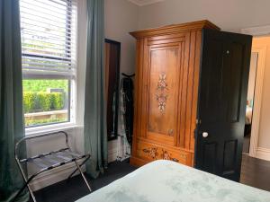 een slaapkamer met een houten kast en een stoel naast een raam bij Roslyn Business Studio - 2 bedroom in Dunedin