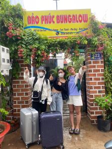 3 personnes portant des masques debout sous un panneau avec bagages dans l'établissement Bảo Phúc Bungalow- Đảo Phú Quý, à Cu Lao Thu